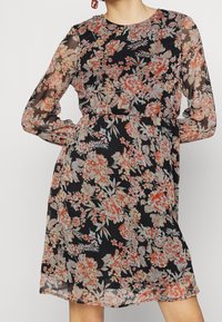 Schwarzes Blümchenkleid mit langen transparenten Ärmeln, verziert mit einer Vielzahl bunter Blumen. Weicher Stoff, tailliert mit einem luftigen Rock.