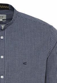 Chemise à rayures verticales bleu marine et blanc avec col mao et boutons blancs, taille moyenne, avec un petit logo brodé sur la poitrine.