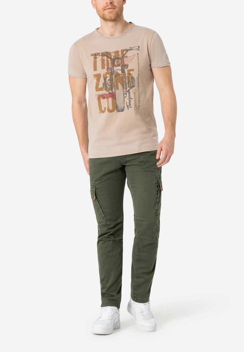 Beige graphic t-shirt met ronde hals, korte mouwen en bedrukking. Olijfgroene cargobroek met ritszakken en tapered fit.