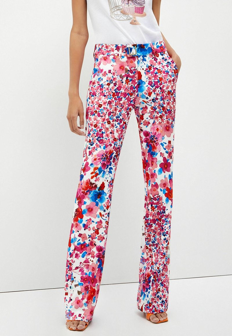 Pantalon à jambes larges à motif floral en rose, rouge, bleu et blanc, assorti à des talons ouverts orange et un haut graphique blanc.