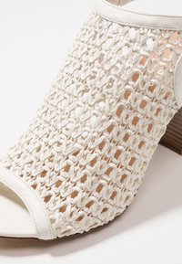 Bílé tkané sandály s otevřenou špičkou a masivním dřevěným podpatkem, s texturovaným tkaným svrškem a hladkými koženými detaily na okraji.