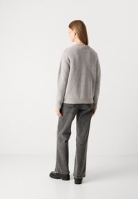 Gray knit sweater with ribbed texture, round neckline, and subtle detailing. Paired with gray denim pants and black platform shoes.