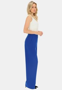 Spodnie niebieskie z wysokim stanem o dopasowanym kroju, z kieszeniami z przodu, gładką fakturą i gładkim wykończeniem. Stylizowane z białą bluzką.