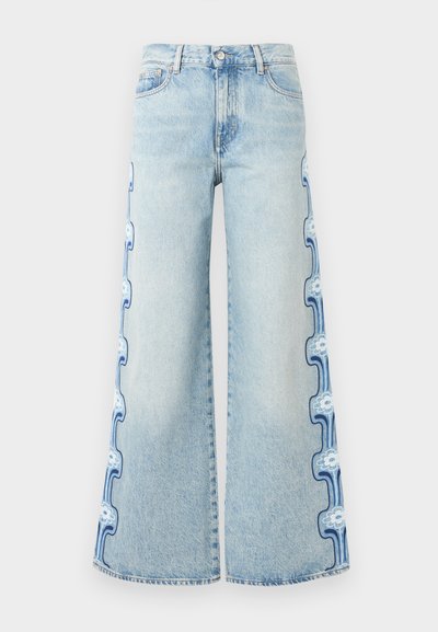 Φαρδιά τζιν σε ανοιχτό μπλε με κεντήματα λουλουδιών και κυμάτων κατά μήκος των εξωτερικών ραφών από τη μέση μέχρι το τελείωμα.