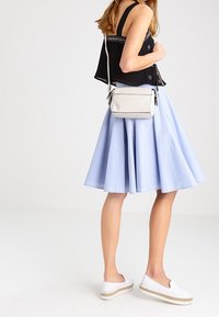 Donna che indossa un top nero senza maniche, una gonna A-line blu chiaro, scarpe bianche slip-on e porta una piccola borsa a tracolla bianca.