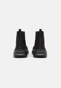 Black ankle boots with a textured knit upper and smooth rubber sole. Features a pull tab at the back for easy wear.