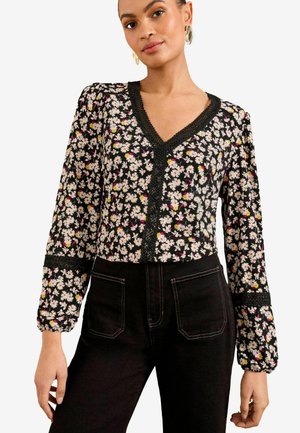 Blouse noire à fleurs avec de longues manches bouffantes, décolleté en V et finition en dentelle. Présente des motifs floraux blancs, roses et jaunes sur un fond sombre.
