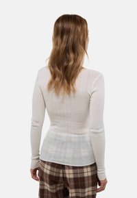 Pull beige ajusté à côtes avec des manches longues, finition texturée et un matériau doux et extensible, assorti à un pantalon à carreaux marron.