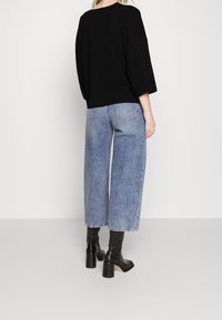 Czarny, oversize'owy sweter z opuszczonymi ramionami, zestawiony z szerokimi, jasnoniebieskimi jeansami. Całość dopełniają czarne botki na obcasie.