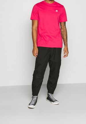 Rosa Baumwoll-T-Shirt mit kurzen Ärmeln und kleinem weißem Logo auf der Brust, kombiniert mit schwarzen Cargohosen und schwarzen High-Top-Sneakern.