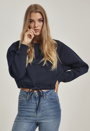 Navy cropped sweatshirt with long sleeves, textured fabric, ribbed cuffs, and drawstring hem. Paired with light blue high-waisted jeans.