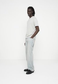 Lys grå v-hals t-skjorte, avslappede lyseblå jeans med falmede områder, og svarte sko. Enkel design, myk tekstur og avslappet stil.