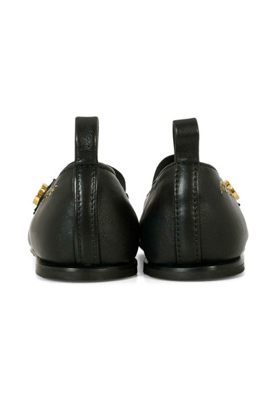 Des chaussures en cuir noir avec une texture lisse, un bout arrondi et des accents en or proéminents. Deux tirettes sont situées au niveau du talon.