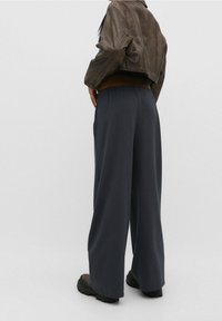 Pantalones de pierna ancha en tela gris oscuro con textura suave, con cintura elástica y combinados con un top marrón y botas marrones.