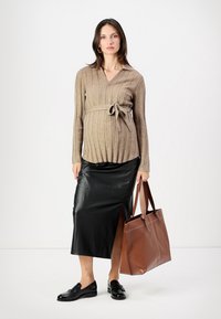 Beige gerippter Pullover mit Bindegürtel, schwarzer Kunstlederrock mit Schlitz an der Seite, schwarze Schuhe und braune Tote-Tasche mit strukturiertem Design.