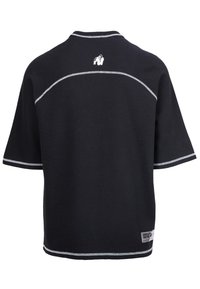 Zwarte T-shirt met korte mouwen, met een ribbelstructuur, witte stiksels langs de naden en een klein logo op de achterkant bij de halslijn.