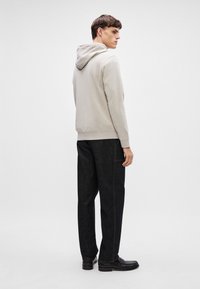 Vaaleanharmaa huppari, jossa on pehmeä kangas ja huppu, yhdistetty tummiin farkkuihin ja mustiin jalkineisiin. Malli seisoo sivuprofiilissa.