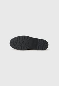 Schwarze Gummisohle mit einer strukturierten Oberfläche, die kreisförmige und lineare Profilmuster für besseren Grip aufweist. Elegantes Design mit abgerundeten Kanten.
