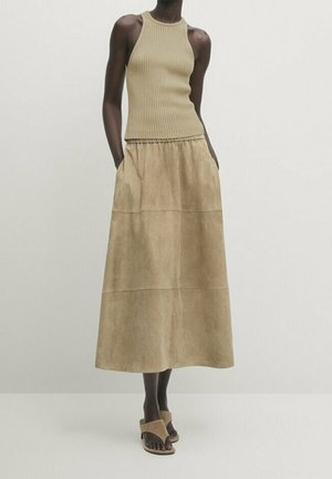 Woman wearing a sleeveless ribbed beige top, high-waisted beige midi skirt with pockets, and beige open-toe heeled sandals.