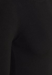 Gros plan sur un tissu noir à côtes montrant des lignes texturées verticales et une couture courbée.