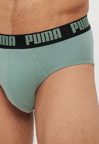 PUMA herrebrief i dempet grønn med svart elastisk midje som har grå logo-tekst. Mykt stoff med en glatt, tettsittende design.