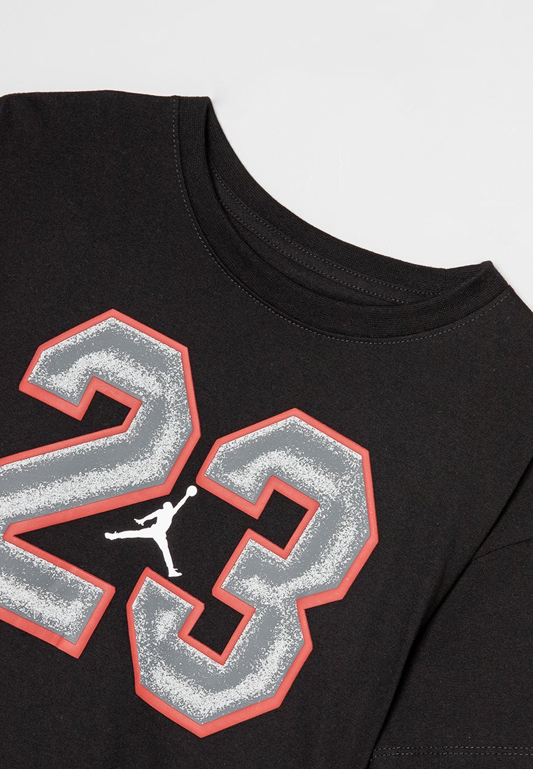 Camiseta de algodón negra con cuello redondo, que presenta un gran "23" gris con contorno rojo y un logo Jumpman blanco entre los números.