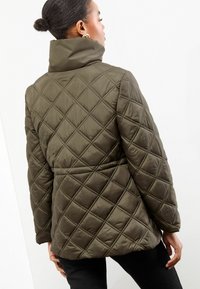 Gevulde jas in olijfgroen, met een hoge kraag, geometrische ruitstiksels en een getailleerde bustehouder met een op maat gemaakte taille.