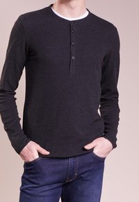 Mörkgrå långärmad henley-tröja av ribbat tyg; har en rund halsringning och en tre-knappars knappslå på framsidan.