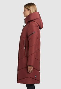 Maroon puffer coat with a high collar and hood, featuring diagonal quilted pattern, zippered pockets, and black hardware accents.