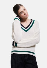 Weißer Strickpullover mit V-Ausschnitt, versehen mit grünen und marineblauen Streifen am Ausschnitt und an den Bündchen. Leichter, strukturierter Stoff und lässige Passform.