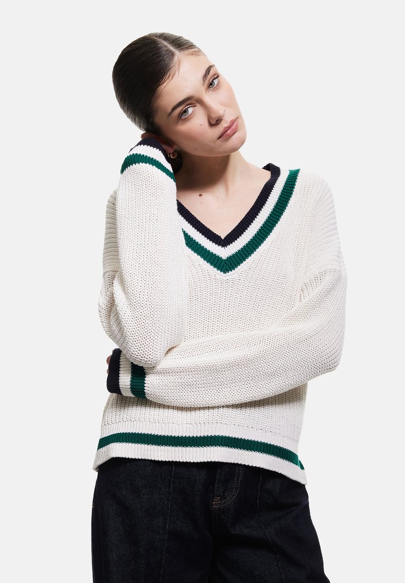 Weißer Strickpullover mit V-Ausschnitt, versehen mit grünen und marineblauen Streifen am Ausschnitt und an den Bündchen. Leichter, strukturierter Stoff und lässige Passform.