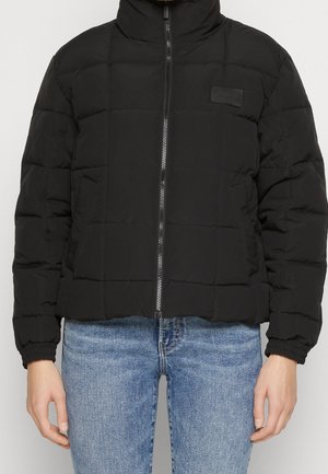 Black puffer jacket with a high collar, zip closure, and quilted design. Features elastic cuffs and a small logo patch on the chest.
