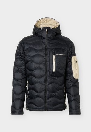 Sort quiltet dunjakke med beige foring i hætten, brystlomme og armlomme, med lynlås foran og Peak Performance-logo på brystlommen.