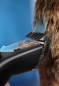 Haartrimmer met een zwart ergonomisch handvat, transparante behuizing en precisiebladen die bruin haar knippen. Opvallend is de heldere beschermkap.