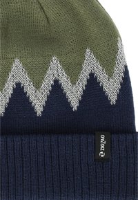 Strikket beanie i olivengrøn og marineblå, med et zigzag-mønster i hvid. Inkluderer et sort mærke med "ZIGZAG" på kanten.