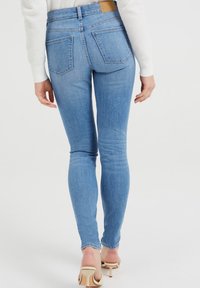 Úzké džíny ve světle modrém denimu, s vysokým pasem, designem pěti kapes a detailem na zadním dílu. Nosené s bílým texturovaným svetr.