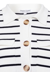 Weißes Strickshirt mit schwarzen Streifen, ausgestattet mit einem Kragen, zwei vorderen Taschen und großen braunen Knöpfen zum Verschließen.