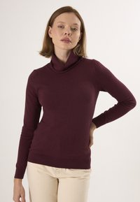 Burgundowa sweter z kołnierzem o długich rękawach, luźnym kroju oraz ściągaczami u mankietów i na dolnej krawędzi, wykonany z miękkiego, elastycznego materiału.