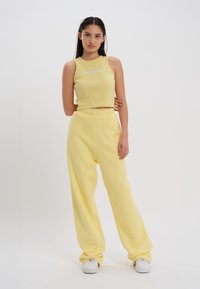 Gul ribbet crop topp med brodert tekst, sammen med matchende vide bukser. Materialet ser mykt og teksturert ut. Hvite sneakers fullfører stilen.