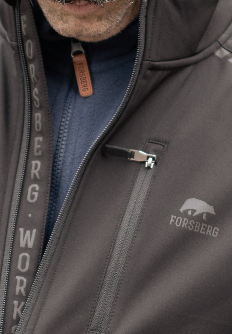 Schwarze Softshelljacke mit einer zipbaren Brusttasche, grauen Akzenten und Logodetails. Hergestellt aus strapazierfähigem Material mit einer glatten Textur.