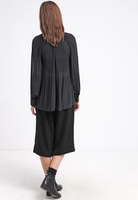 Czarna plisowana bluzka z długimi rękawami, o zwiewnym kroju i przezroczystych panelach. Do tego szerokie czarne kuloty i botki za kostkę.