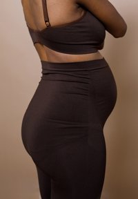 Bruine geribbelde bralette met verstelbare bandjes en hoge bruine leggings, die een zachte textuur en aansluitende silhouet benadrukken.