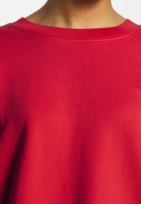 Czerwona, prążkowana bawełniana bluza z szerokim dekoltem i subtelnym logo. Posiada krótkie, luźne rękawy oraz gładką fakturę.