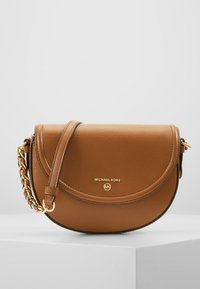 Brun læder crossbody taske med et buet design, guld hardware, en kæde-strop og prægede logo på forsiden. Teksturområde detaljer til stede.