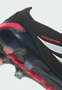 Μαύρο αθλητικό παπούτσι με υφασμάτινο επάνω μέρος με υφή, διαφανές πάτο με κόκκινες λεπτομέρειες και λογότυπο «PREDATOR» σε κόκκινο. Διαθέτει ευέλικτα σχεδιαστικά στοιχεία.