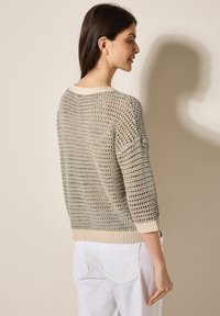 Pull léger en maille ouverte gris et beige, avec des manches trois-quarts et un col en côtes. Motif texturé aux tons neutres.