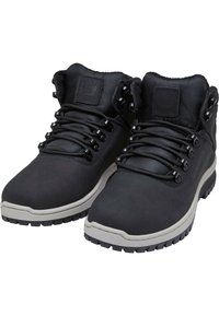 Botas de senderismo negras con parte superior de cuero suave, collar acolchado y lengüeta texturizada con ojales metálicos y suela de goma.