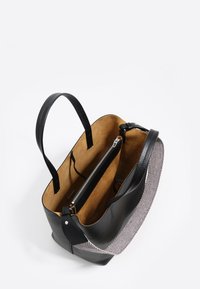 Czarna skórzana torba na ramię z brązowym zamszowym wnętrzem, wewnętrzną kieszenią na zamek oraz dwoma uchwytami, częściowo odsłonięta tkanina w pepitkę na zewnętrznej stronie.