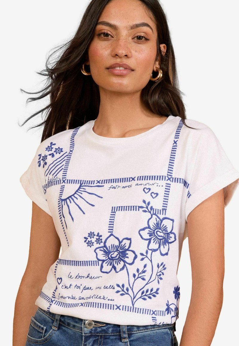 Tricou alb din bumbac cu broderie florală albastră, mâneci scurte și decolteu rotund. Are cusături decorative și text scris de mână.
