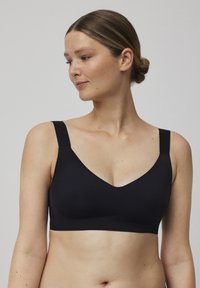 Sujeción inalámbrica negra con escote en V, tirantes anchos y textura de tela suave. Diseñada para la comodidad sin detalles de hardware visibles.